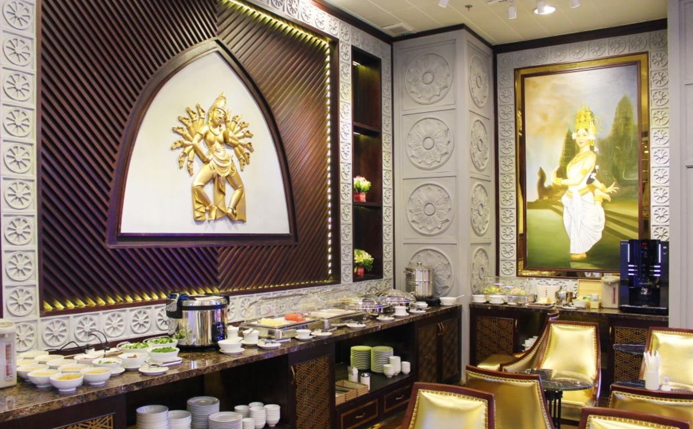 "Buffet dining area at The Champ Lounge, Cam Ranh International Airport, with hot food, rice, and soup stations under ornate wall décor featuring a golden sculpture and traditional artwork.