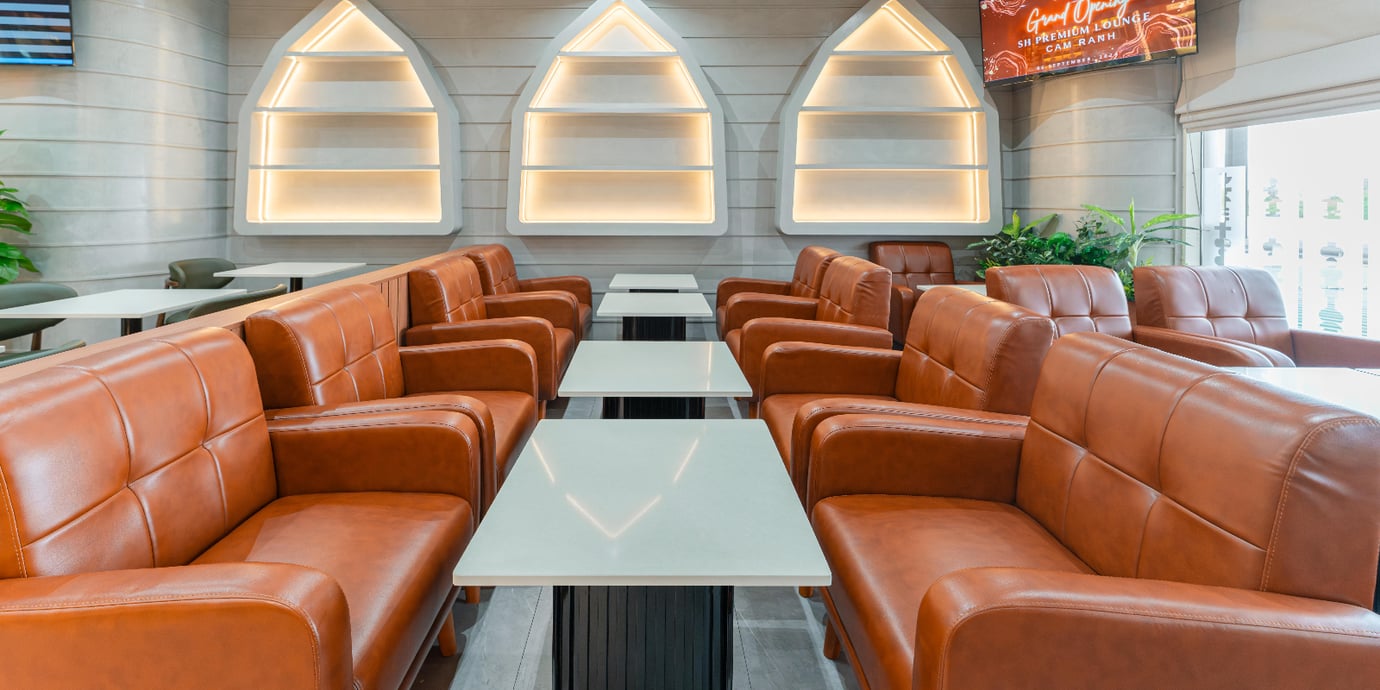 Dining area at SH Premium Lounge, Cam Ranh International Airport Terminal 1, featuring rows of brown leather armchairs and marble tables in a modern lounge setting.