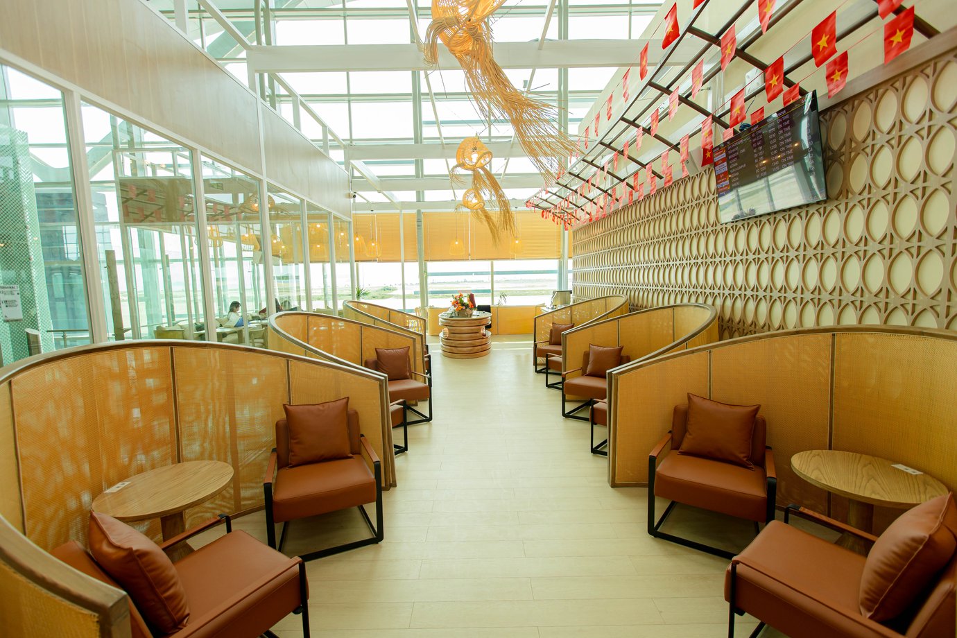 Private seating pods with cushioned chairs and wooden tables at SH Premium Lounge, Cam Ranh International Airport Terminal 2, featuring modern rattan design and natural light from floor-to-ceiling windows.