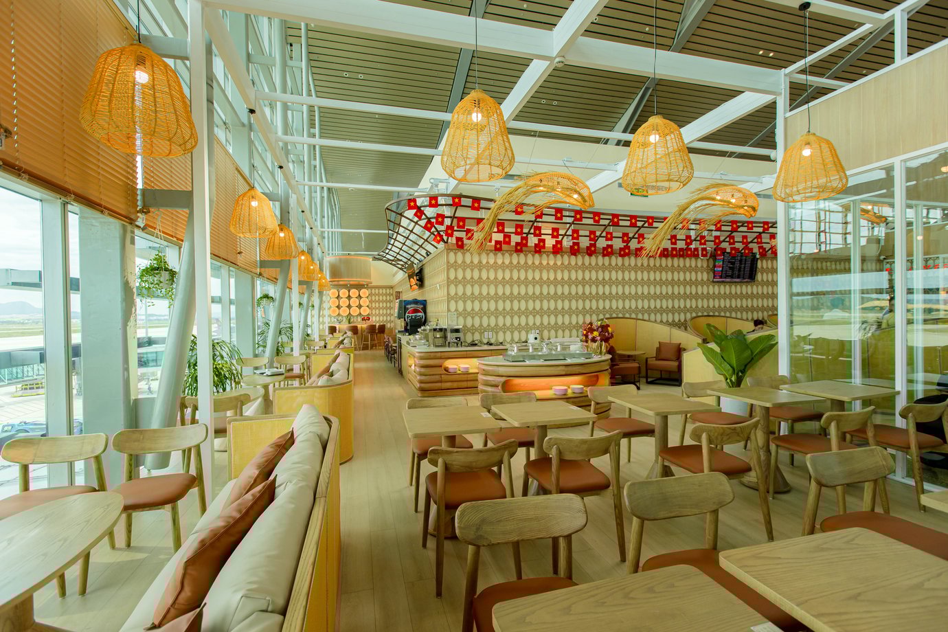Seating and dining area at SH Premium Lounge, Cam Ranh International Airport Terminal 2, featuring modern wooden furniture, pendant lighting, and panoramic runway views.