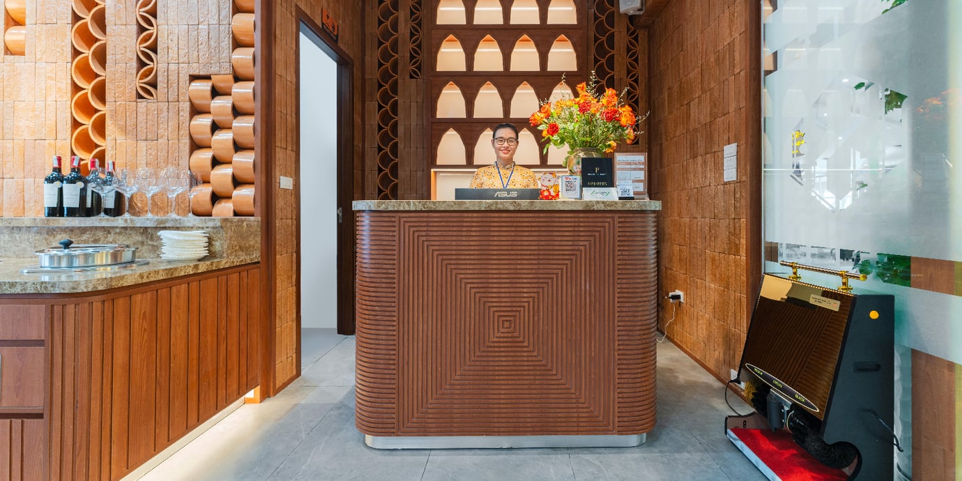 Reception counter at SH Premium Lounge in Cam Ranh International Airport Terminal 1, featuring elegant wooden interiors, decorative wall design, and a friendly staff member ready to assist guests.