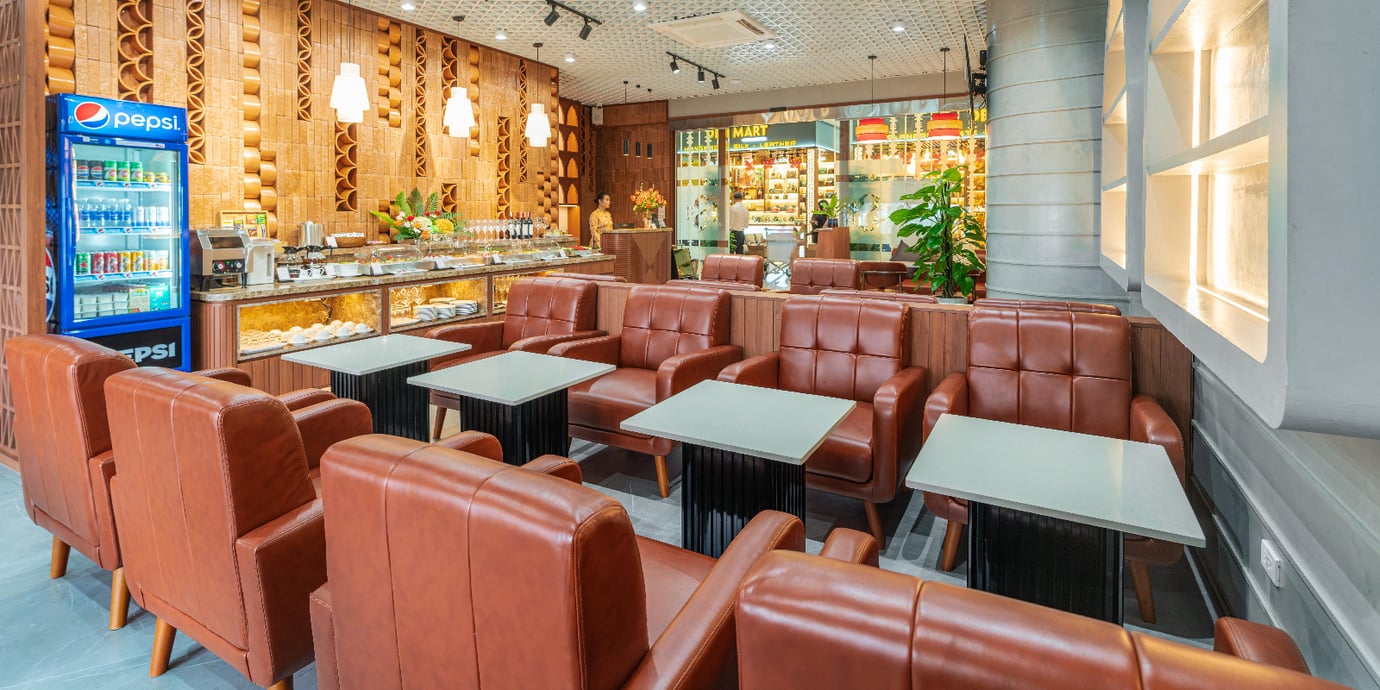 Comfortable leather seating area inside SH Premium Lounge at Cam Ranh International Airport Terminal 1, featuring a buffet counter with drinks and snacks in a modern, wood-accented design.