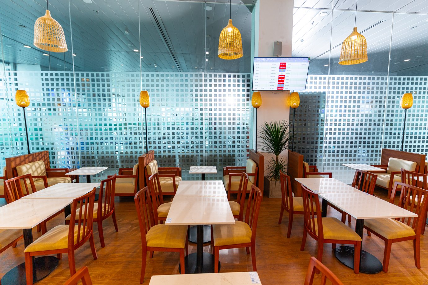 The SH Premium Lounge dining area with marble-top tables, wood chairs, cushioned booth seating, woven pendant lights, and floor-to-ceiling glass walls overlooking the terminal.