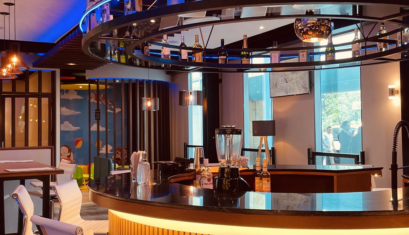 The Lounge T3 at Cancun International Airport bar area with circular bar counter, overhead bottle display, and ambient lighting with seating nearby. The Lounge T3 at Cancun International Airport bar area with circular bar counter, overhead bottle display, and ambient lighting with seating nearby.