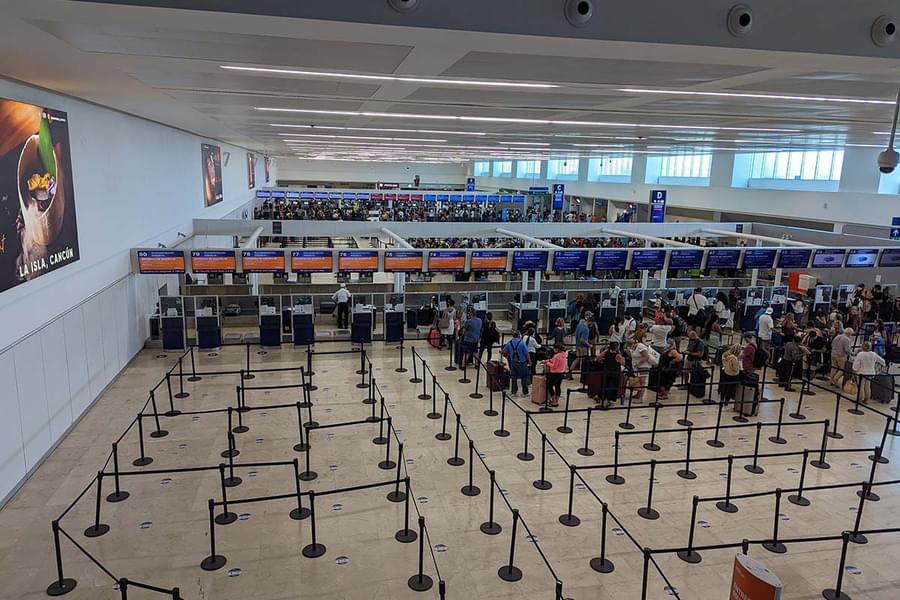 Cancun International Airport check-in hall with airline counters, queue lines, and passengers waiting in a large departures area. Cancun International Airport check-in hall with airline counters, queue lines, and passengers waiting in a large departures area.
