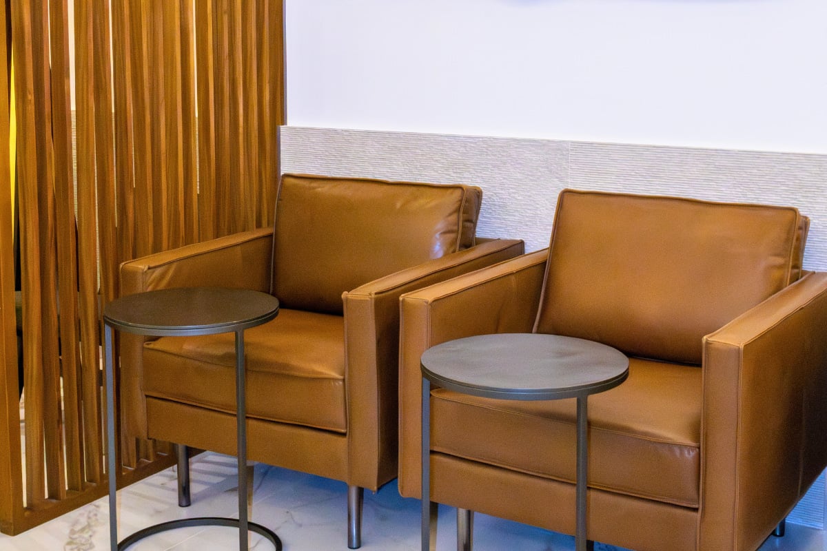 Two tan leather armchairs with matching black round side tables, positioned next to a wooden slat divider in the Mera Roof Lounge. The seating area features a light textured wall and marble-style flooring Two tan leather armchairs with matching black round side tables, positioned next to a wooden slat divider in the Mera Roof Lounge. The seating area features a light textured wall and marble-style flooring