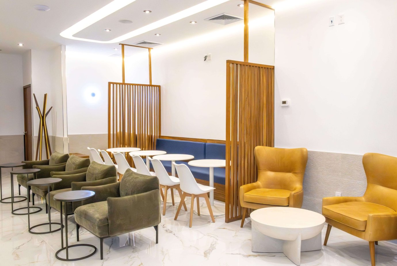 VIP Lounge by Mera at Cancun International Airport seating area with armchairs, round tables, dining chairs, booth seating, and wooden partition screens. VIP Lounge by Mera at Cancun International Airport seating area with armchairs, round tables, dining chairs, booth seating, and wooden partition screens.