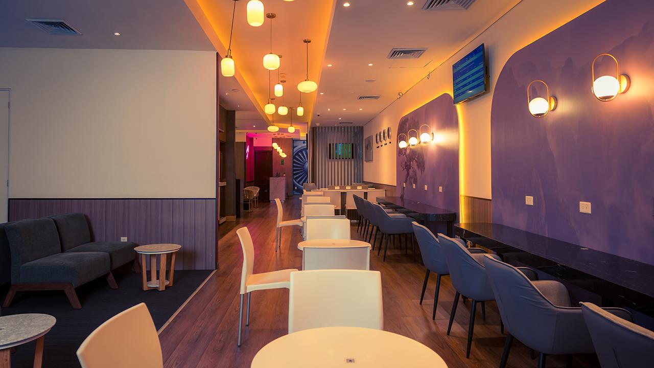 The Lounge T2 at Cancun International Airport seating area with dining tables, bar-style seating, and ambient lighting in a modern lounge space. The Lounge T2 at Cancun International Airport seating area with dining tables, bar-style seating, and ambient lighting in a modern lounge space.