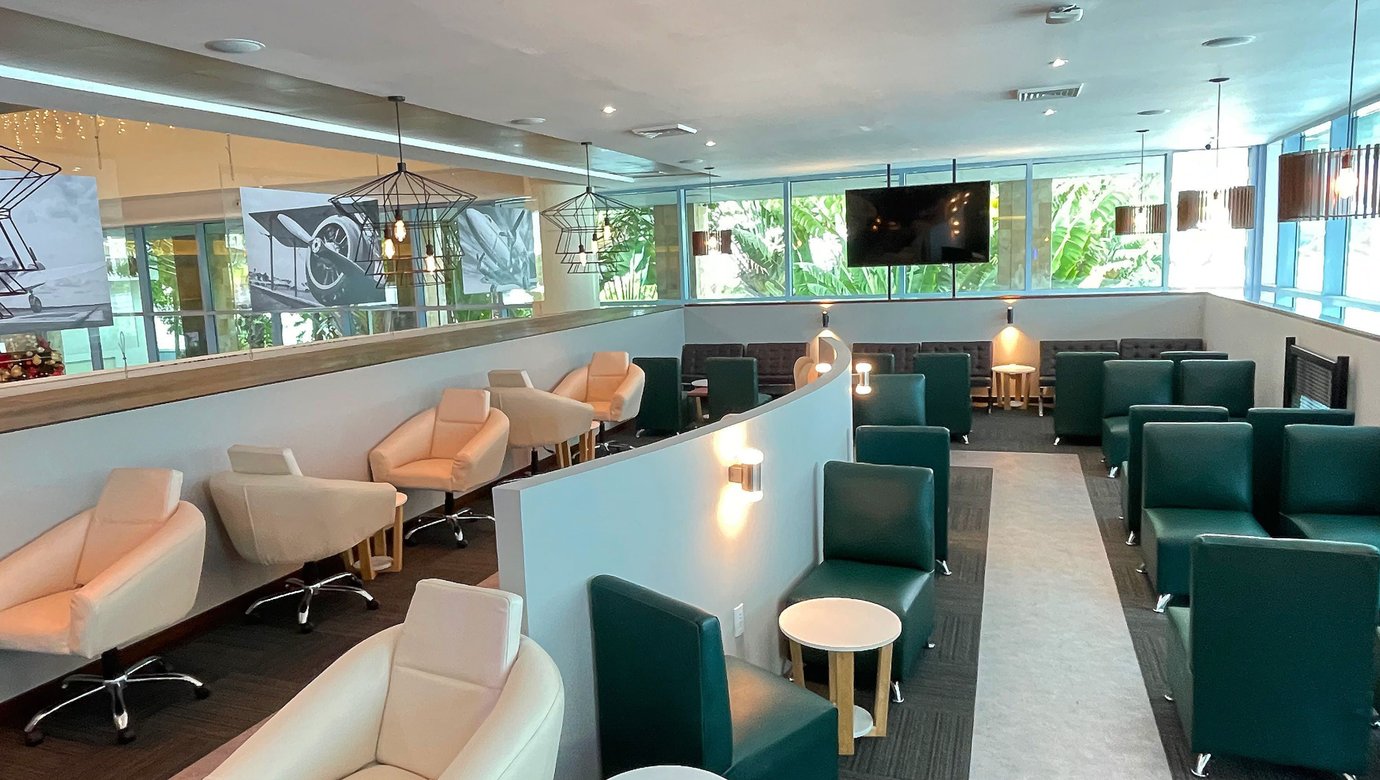 The Lounge T3 at Cancun International Airport seating area with lounge chairs, side tables, partitioned seating sections, and large windows with greenery views. The Lounge T3 at Cancun International Airport seating area with lounge chairs, side tables, partitioned seating sections, and large windows with greenery views.