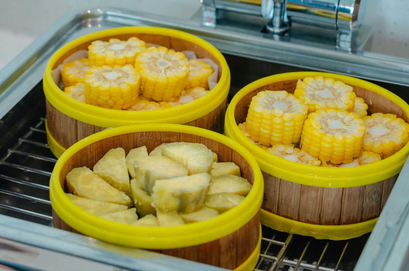 Steamed corn slices and sweet potatoes served in bamboo-style containers on a hot food station at SH Premium Lounge, Cat Bi International Airport (HPH).