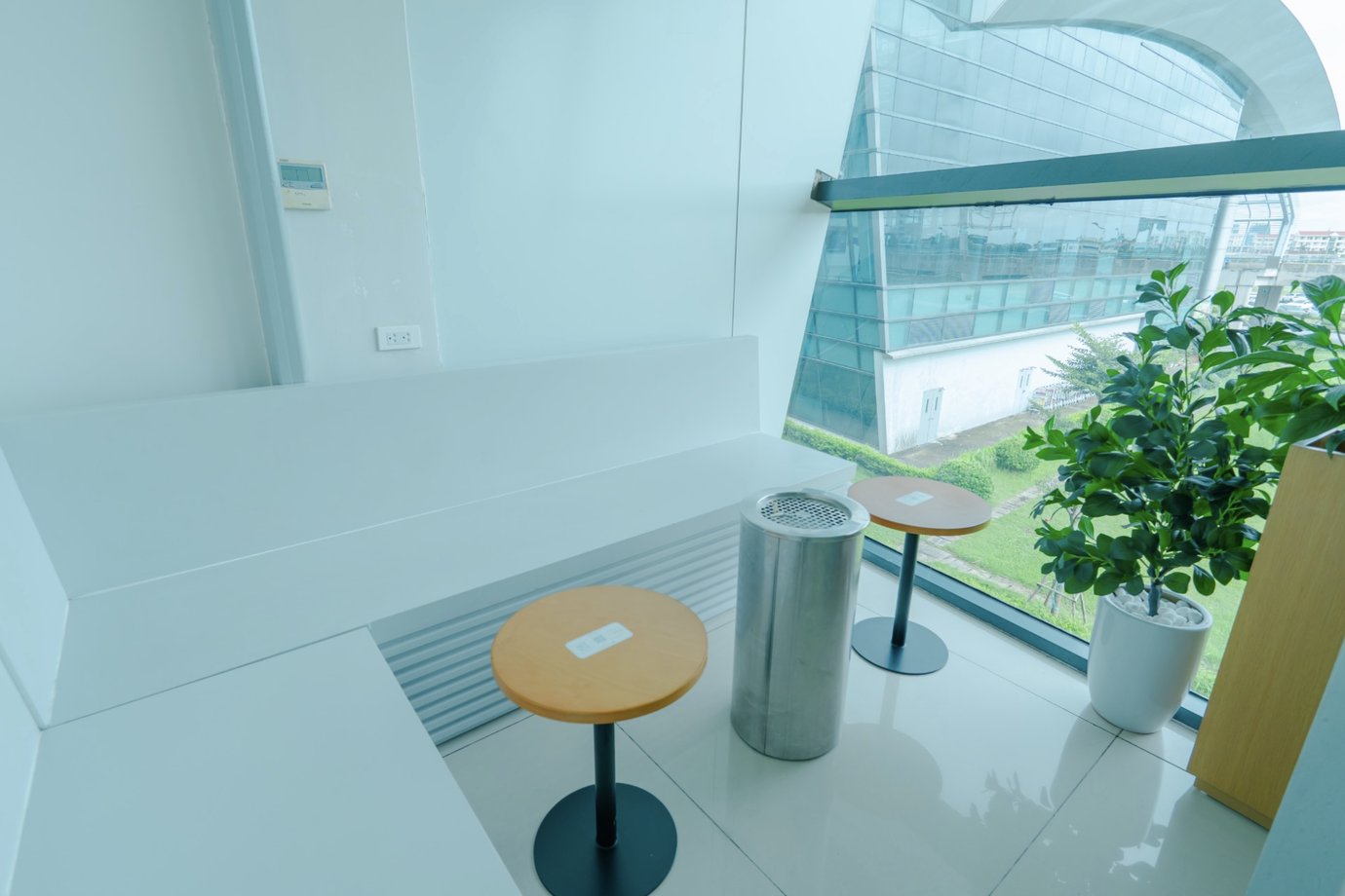 Designated smoking area at SH Premium Lounge, Cat Bi International Airport (HPH), featuring a built-in bench, small round tables, an ashtray bin, and floor-to-ceiling windows overlooking the terminal exterior.