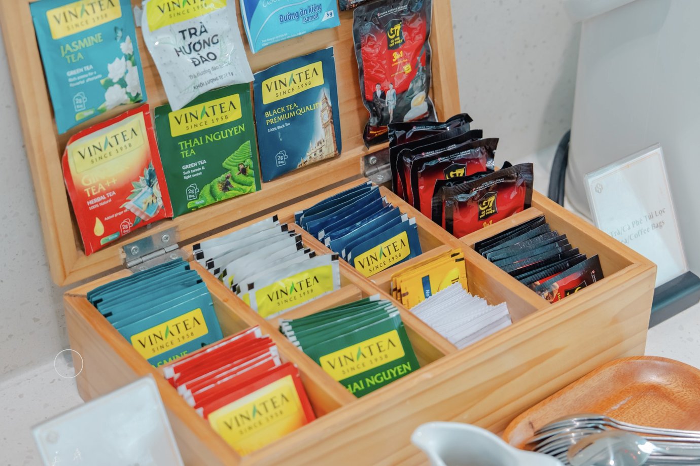 Selection of individually wrapped tea bags displayed in a wooden organizer, including jasmine, green, and black tea options at SH Premium Lounge, Cat Bi International Airport (HPH).