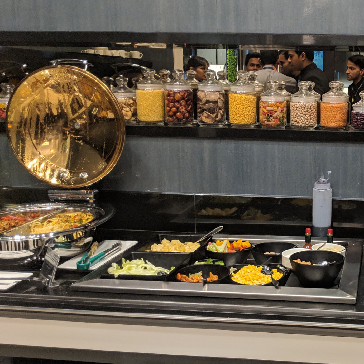 Buffet counter at the Centurion Lounge Mumbai Airport Terminal 2 featuring salads, fresh vegetables, cereals, and hot dishes displayed in glass jars and serving trays. Buffet counter at the Centurion Lounge Mumbai Airport Terminal 2 featuring salads, fresh vegetables, cereals, and hot dishes displayed in glass jars and serving trays.