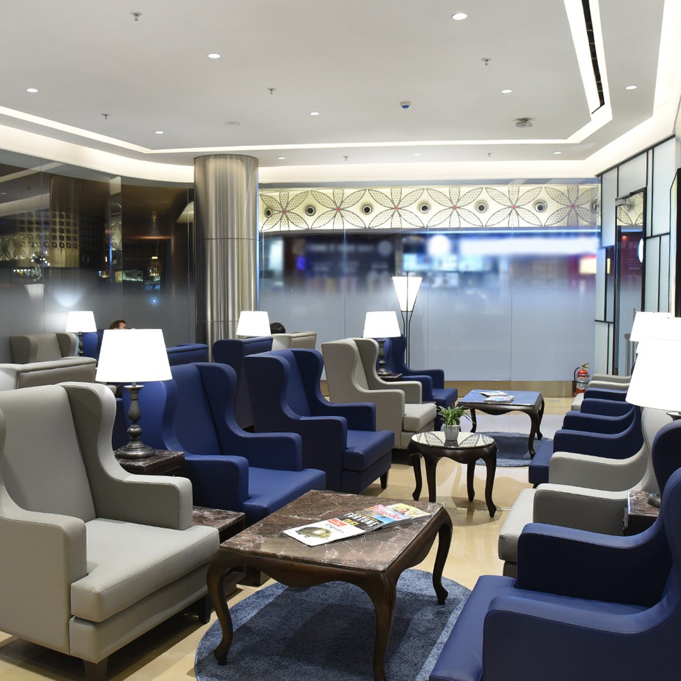 Comfortable armchair seating inside the Centurion Lounge at Mumbai Airport Terminal 2, with blue and grey lounge chairs arranged around marble coffee tables. Comfortable armchair seating inside the Centurion Lounge at Mumbai Airport Terminal 2, with blue and grey lounge chairs arranged around marble coffee tables.