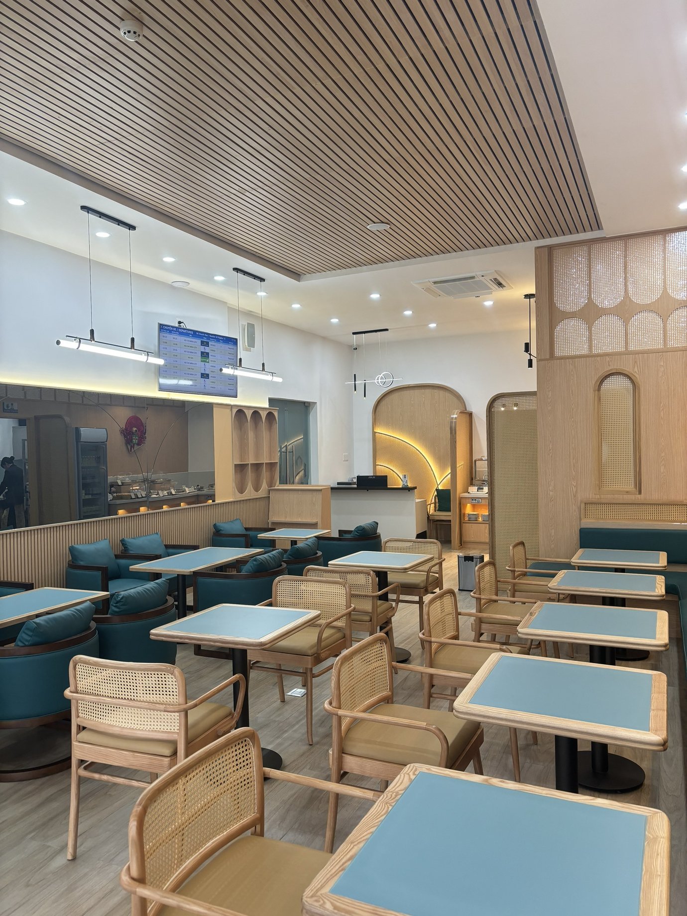 SH Premium Lounge seating area at Con Dao Airport (VCS), showcasing a calm, contemporary interior with natural wood finishes, cane-backed chairs, soft blue tabletops, and warm ambient lighting