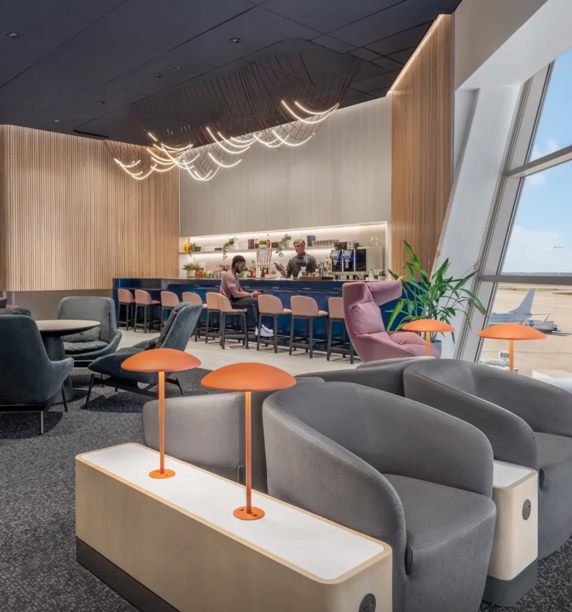 Contemporary seating and bar area inside Capital One Lounge DFW featuring premium lounge chairs, runway views, modern lighting, and a full-service bar. Contemporary seating and bar area inside Capital One Lounge DFW featuring premium lounge chairs, runway views, modern lighting, and a full-service bar.