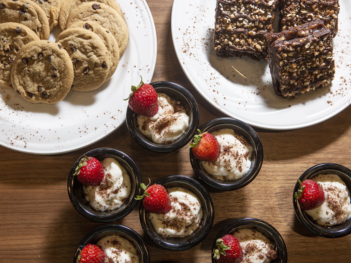 An assortment of desserts and sweet snacks served at the Plaza Premium Lounge at DFW Airport. The spread includes chocolate chip cookies, chocolate oat bars or brownies topped with chopped nuts, and individual cream desserts garnished with fresh strawberries and chocolate shavings. An assortment of desserts and sweet snacks served at the Plaza Premium Lounge at DFW Airport. The spread includes chocolate chip cookies, chocolate oat bars or brownies topped with chopped nuts, and individual cream desserts garnished with fresh strawberries and chocolate shavings.
