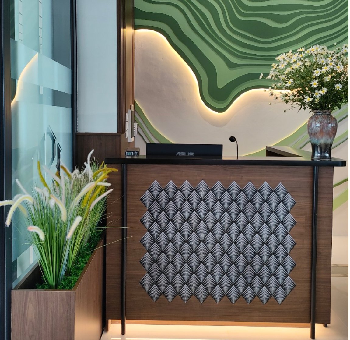 Reception desk at Điện Biên Business Lounge, Điện Biên Phủ Airport (DIN), featuring modern wooden counter, geometric panel design, and green topographic wall backdrop with ambient lighting.