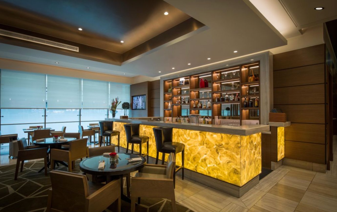 Elegant bar and dining area inside the Ahlan Business Class Lounge at Dubai International Airport Terminal 1, featuring backlit marble counters, comfortable seating, and a modern, warm design for premium travelers. Elegant bar and dining area inside the Ahlan Business Class Lounge at Dubai International Airport Terminal 1, featuring backlit marble counters, comfortable seating, and a modern, warm design for premium travelers.