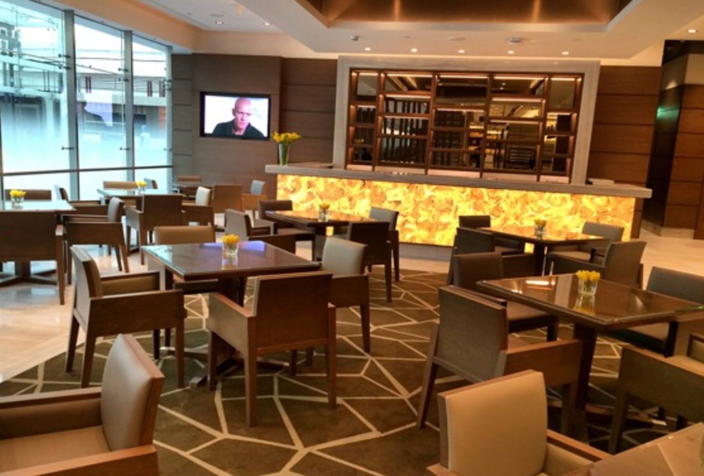 Dining and seating area inside the Lufthansa Business Lounge at Dubai International Airport Terminal 1, featuring elegant wooden furniture, large windows for natural light, and a stylish illuminated bar counter. Dining and seating area inside the Lufthansa Business Lounge at Dubai International Airport Terminal 1, featuring elegant wooden furniture, large windows for natural light, and a stylish illuminated bar counter.
