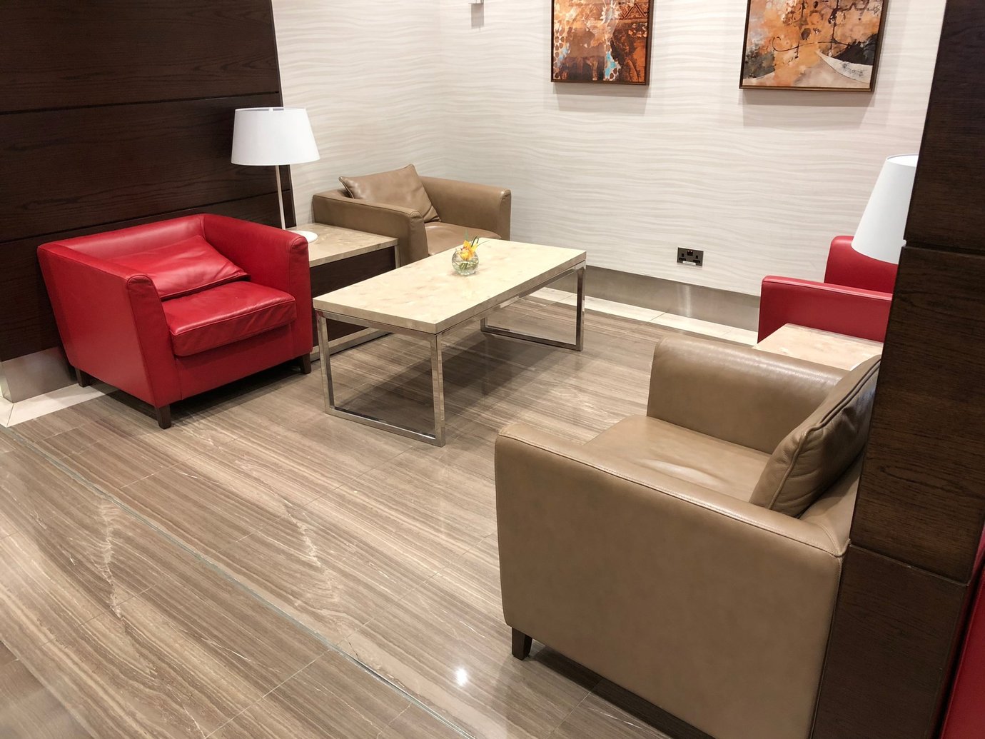 “Private seating corner inside the Marhaba Lounge at Dubai International Airport Terminal 1, featuring red and beige leather armchairs, marble tables, and modern décor for a quiet, comfortable atmosphere. “Private seating corner inside the Marhaba Lounge at Dubai International Airport Terminal 1, featuring red and beige leather armchairs, marble tables, and modern décor for a quiet, comfortable atmosphere.