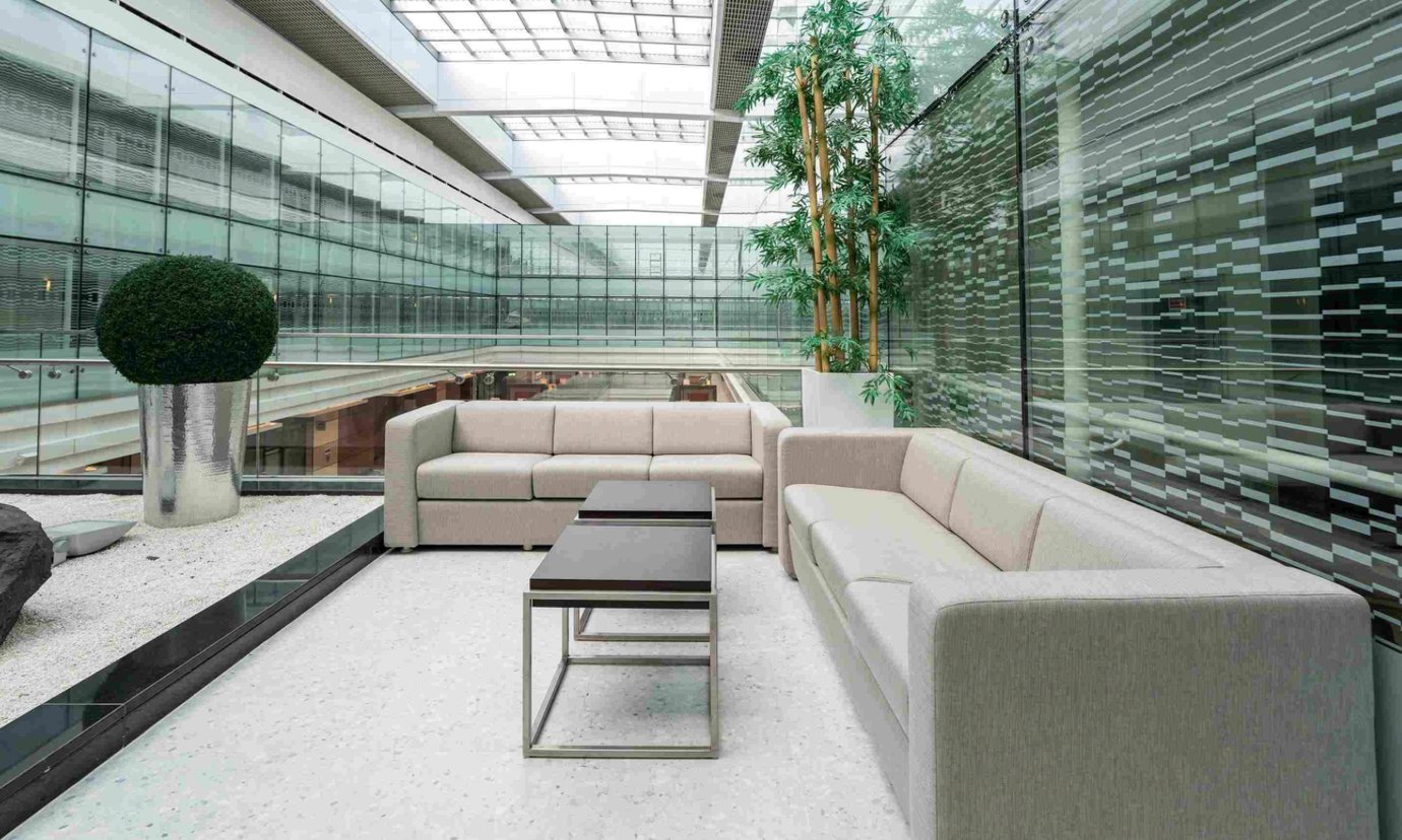 Spacious lounge seating area inside the Ahlan Lounge at Dubai International Airport Terminal 3 Concourse A, featuring modern beige sofas, glass walls, and indoor greenery in a bright, open-air setting.