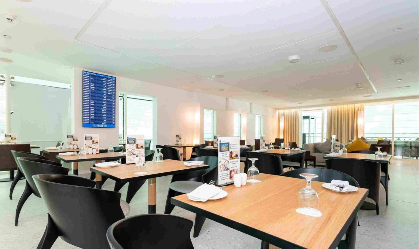 Modern dining area inside the Ahlan Lounge at Dubai International Airport Terminal 3 Concourse A, featuring neatly set tables, soft lighting, and a large digital departures board