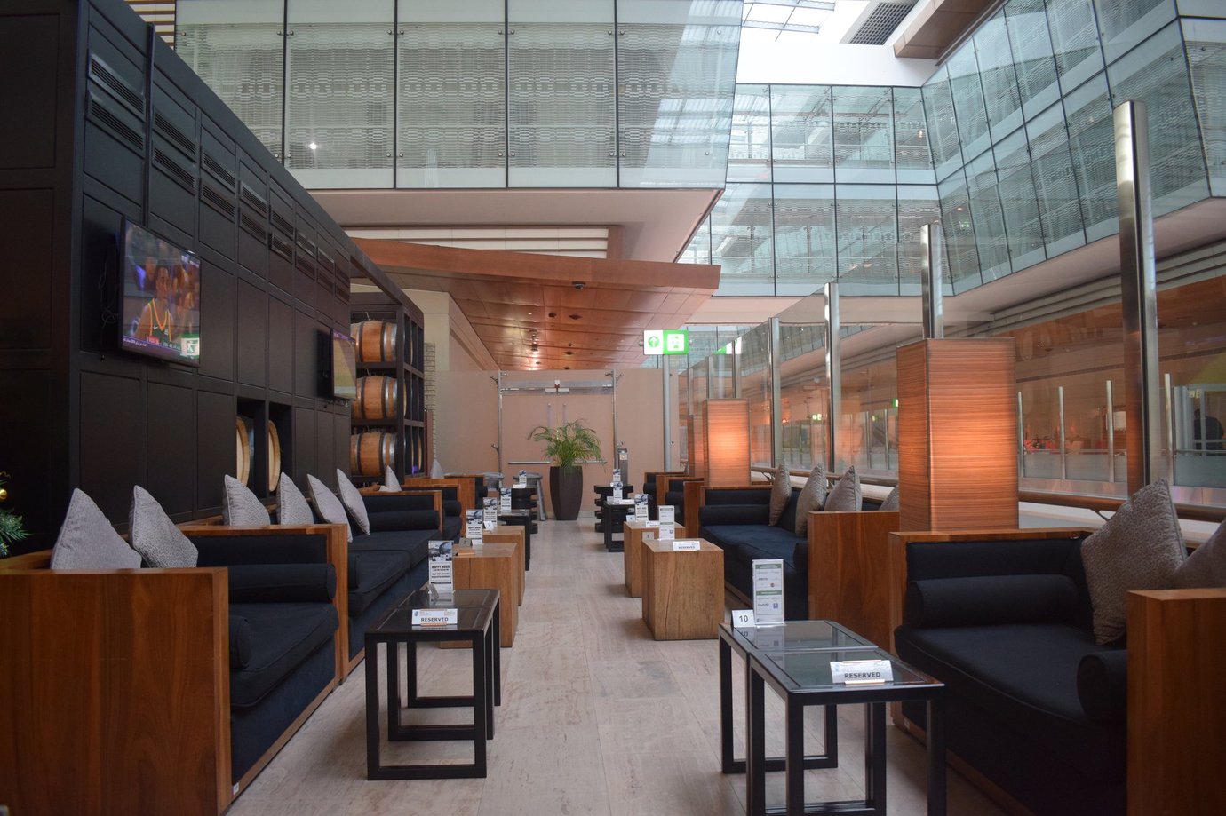 Elegant seating area inside the Ahlan Lounge at Dubai International Airport Terminal 3 Concourse B, featuring wooden furnishings, black sofas with grey cushions, and soft ambient lighting surrounded by glass walls.