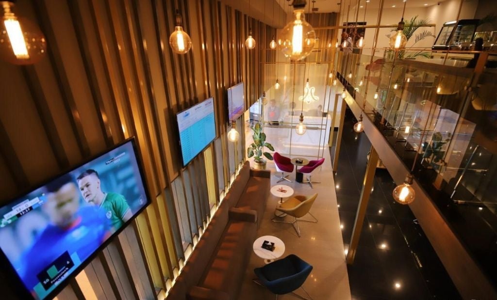 Interior view of Majestic Lounge at Jinnah International Airport (KHI), showcasing modern seating, hanging pendant lights, flight information screens, and a stylish two-level layout for travelers.
