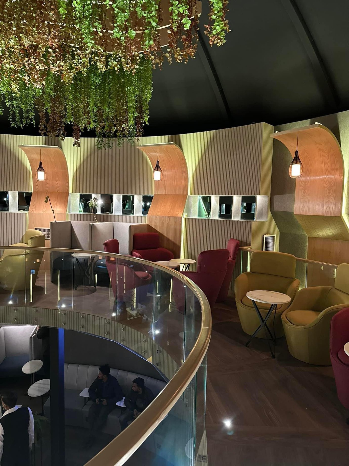 Upper-level seating area at Sky Majestic Lounge, Jinnah International Airport (KHI), featuring curved balcony design, private booths, hanging greenery, and contemporary lounge seating for travelers.