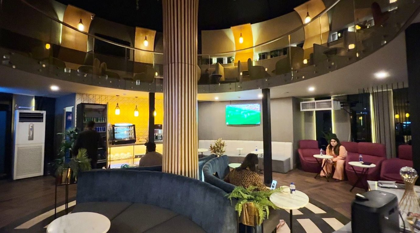 Interior view of Sky Majestic Lounge at Jinnah International Airport (KHI), featuring circular mezzanine seating, modern sofas, TV entertainment area, and relaxed premium lounge ambiance for departing passengers.