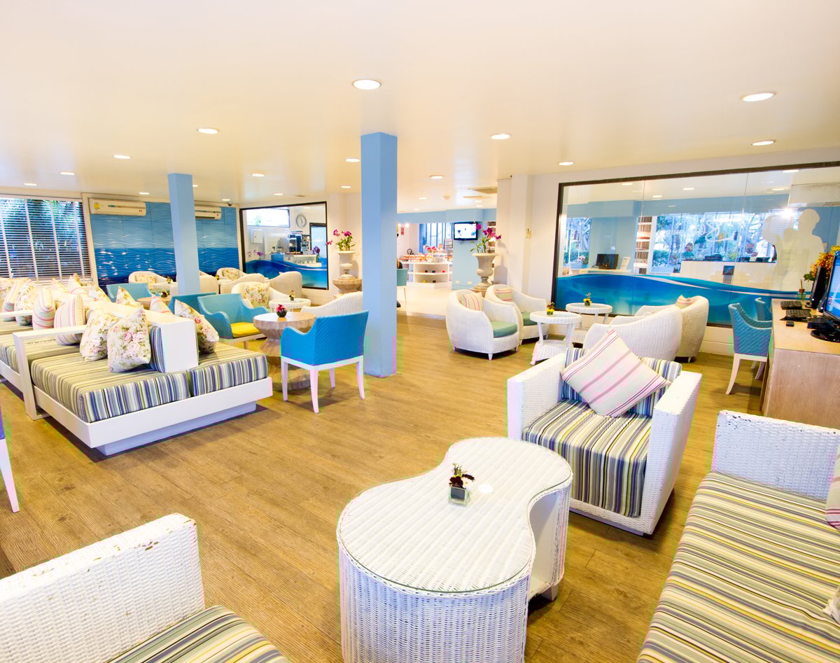 Open seating area at USM Blue Ribbon Lounge (Domestic), featuring white wicker-style armchairs and sofas with striped cushions, small tables, and a refreshment counter in the background.