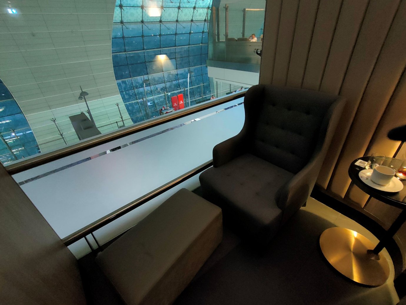 The image shows a private seating area in the Plaza Premium Lounge at DXB, featuring a plush armchair with an ottoman for added comfort. The space is dimly lit, providing a quiet and intimate atmosphere, perfect for relaxation. The image shows a private seating area in the Plaza Premium Lounge at DXB, featuring a plush armchair with an ottoman for added comfort. The space is dimly lit, providing a quiet and intimate atmosphere, perfect for relaxation.