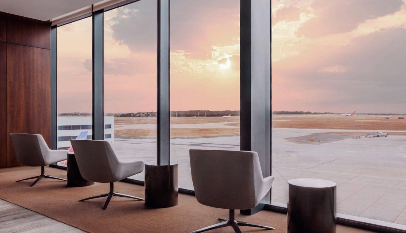 Aspire Lounge seating at Melbourne Airport with armchairs by floor-to-ceiling windows overlooking the runway at sunset.