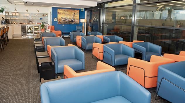 Rex Lounge at Melbourne Airport seating area with rows of armchairs, side tables, and a bar area in the background. Rex Lounge at Melbourne Airport seating area with rows of armchairs, side tables, and a bar area in the background.
