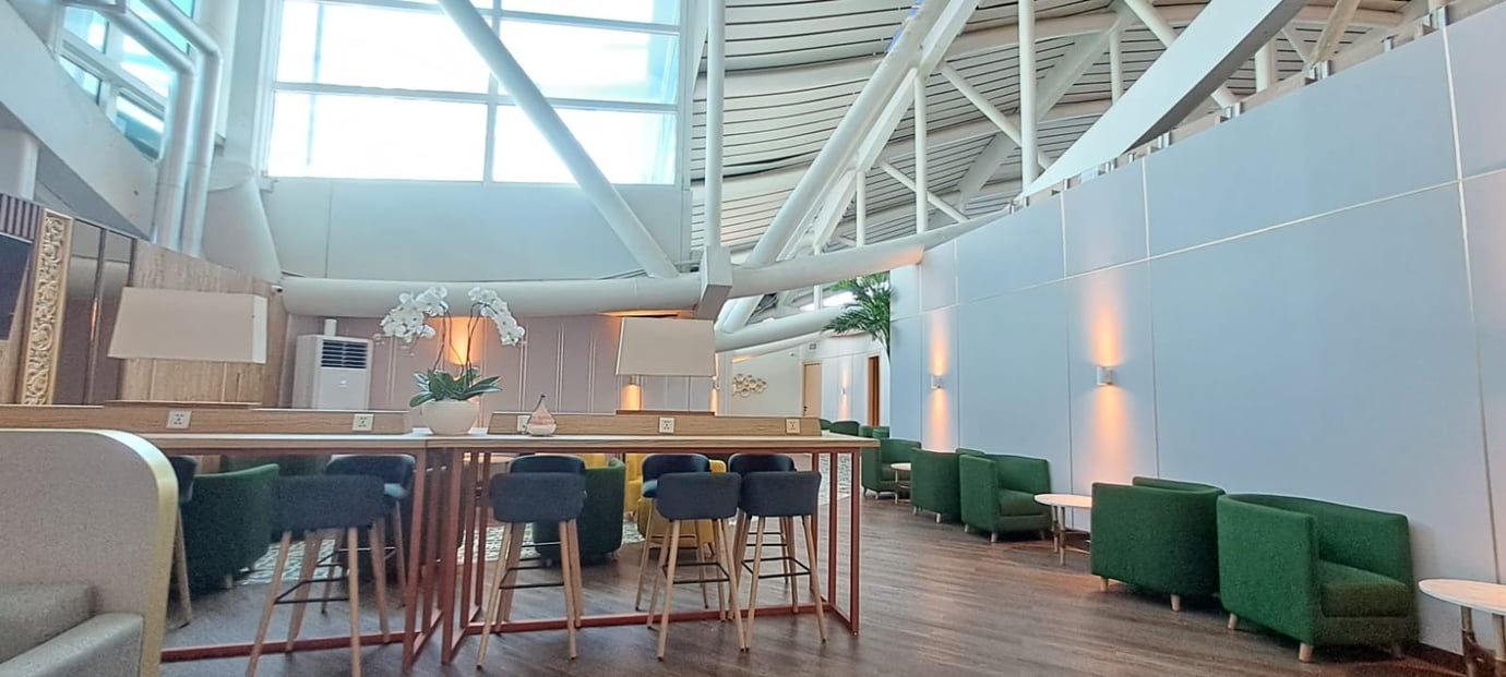 Concordia Lounge seating area at Ngurah Rai International Airport (DPS) Bali with high ceilings, natural light, green armchairs, bar seating, and modern airport lounge workspaces.