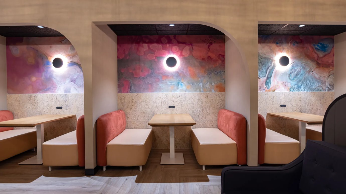 Private booth seating at Aspire Lounge Perth featuring semi-enclosed dining pods with cushioned bench seating, individual tables, ambient wall lighting, and abstract artwork.