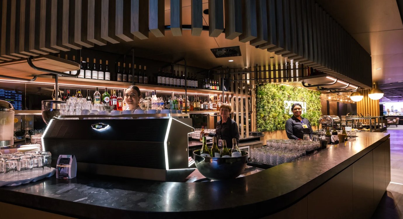 Full-service bar at Aspire Lounge Perth Airport featuring premium wines, spirits, barista coffee, and complimentary beverages served in a modern lounge setting.