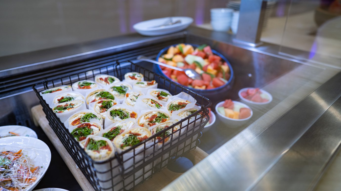 Fresh wraps and cut fruit displayed at the Virgin Australia Lounge Perth buffet counter, including tortilla wraps filled with greens and vegetables, bowls of mixed melon and watermelon, and plated cold dishes