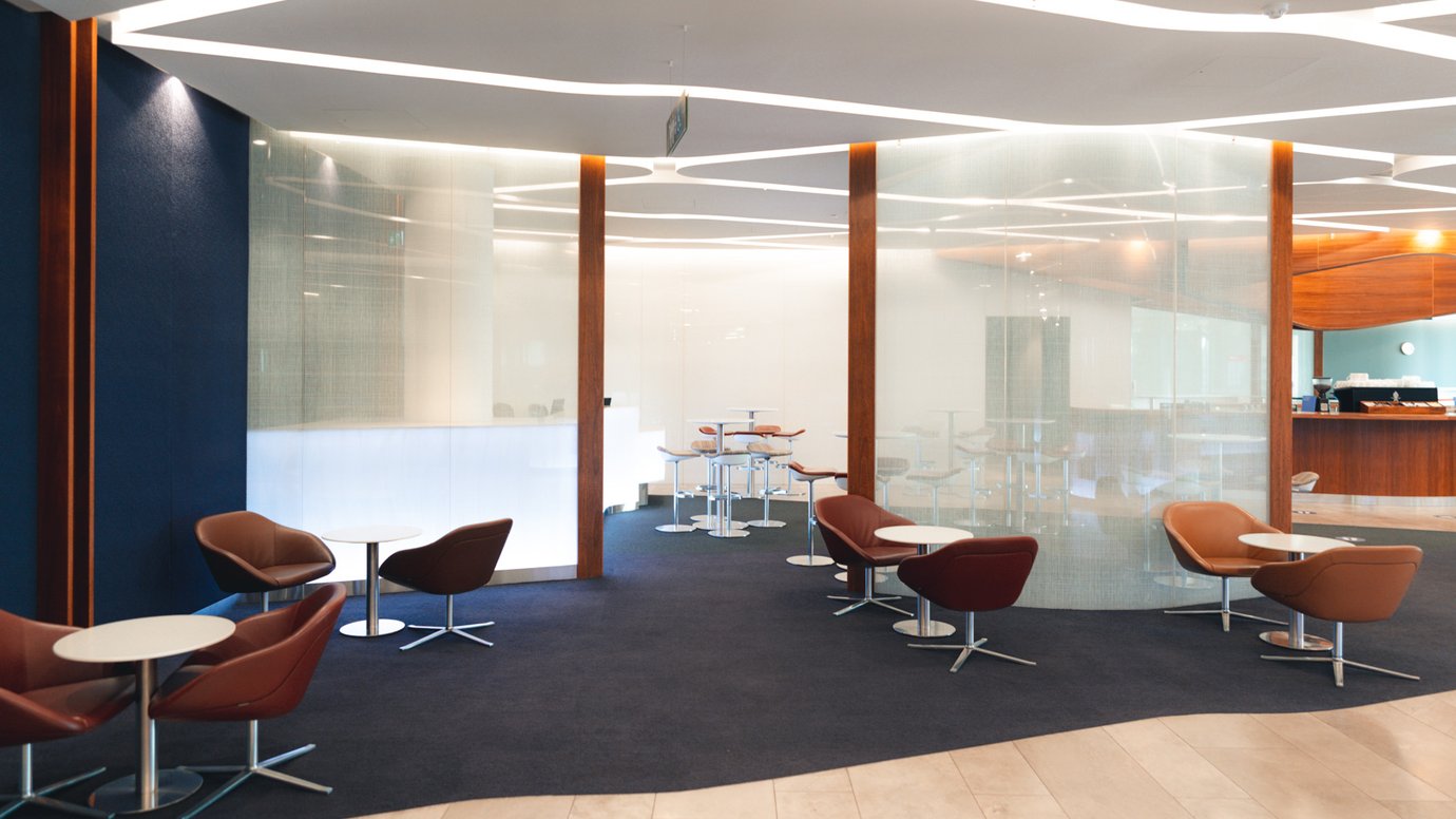 Virgin Australia Lounge Perth seating area with circular café tables, leather lounge chairs, and semi-private seating sections divided by curved frosted glass panels.