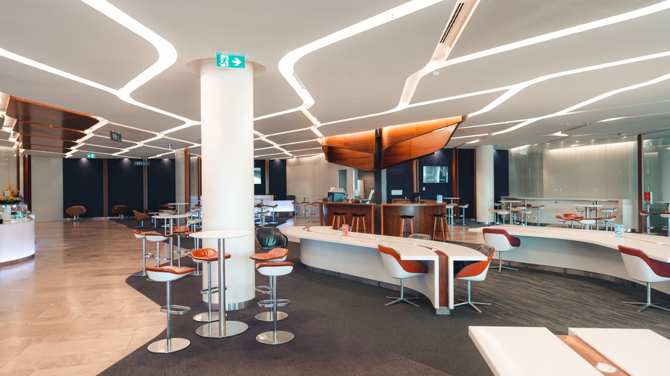 Virgin Australia Lounge Perth seating area with curved communal workstations, high-top tables, and red-and-white leather bar stools.