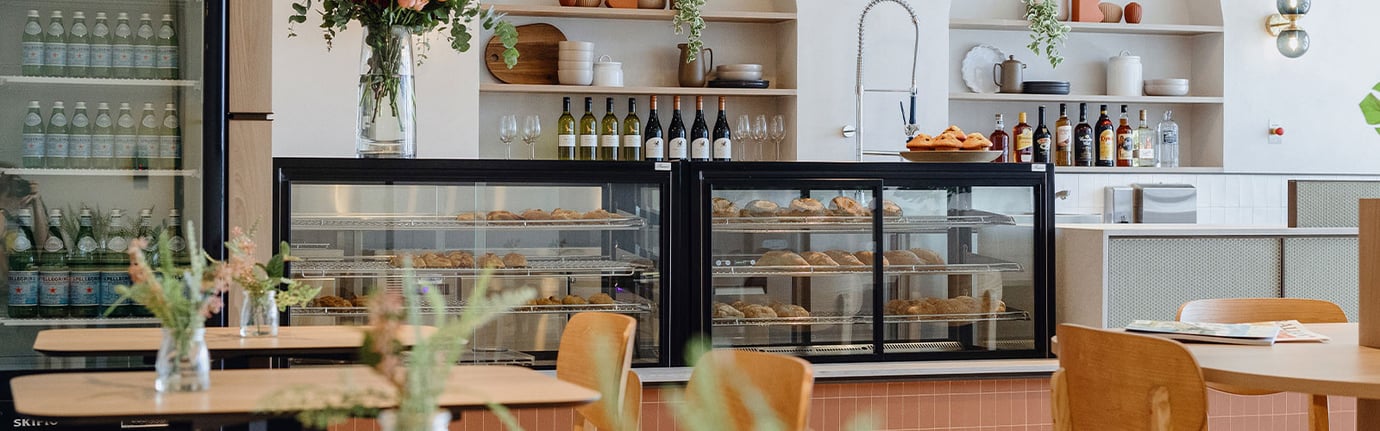 Plaza Premium Lounge at Sydney Airport café area with pastry display cabinets, fresh baked goods, and a bar with wine and beverages in the background.