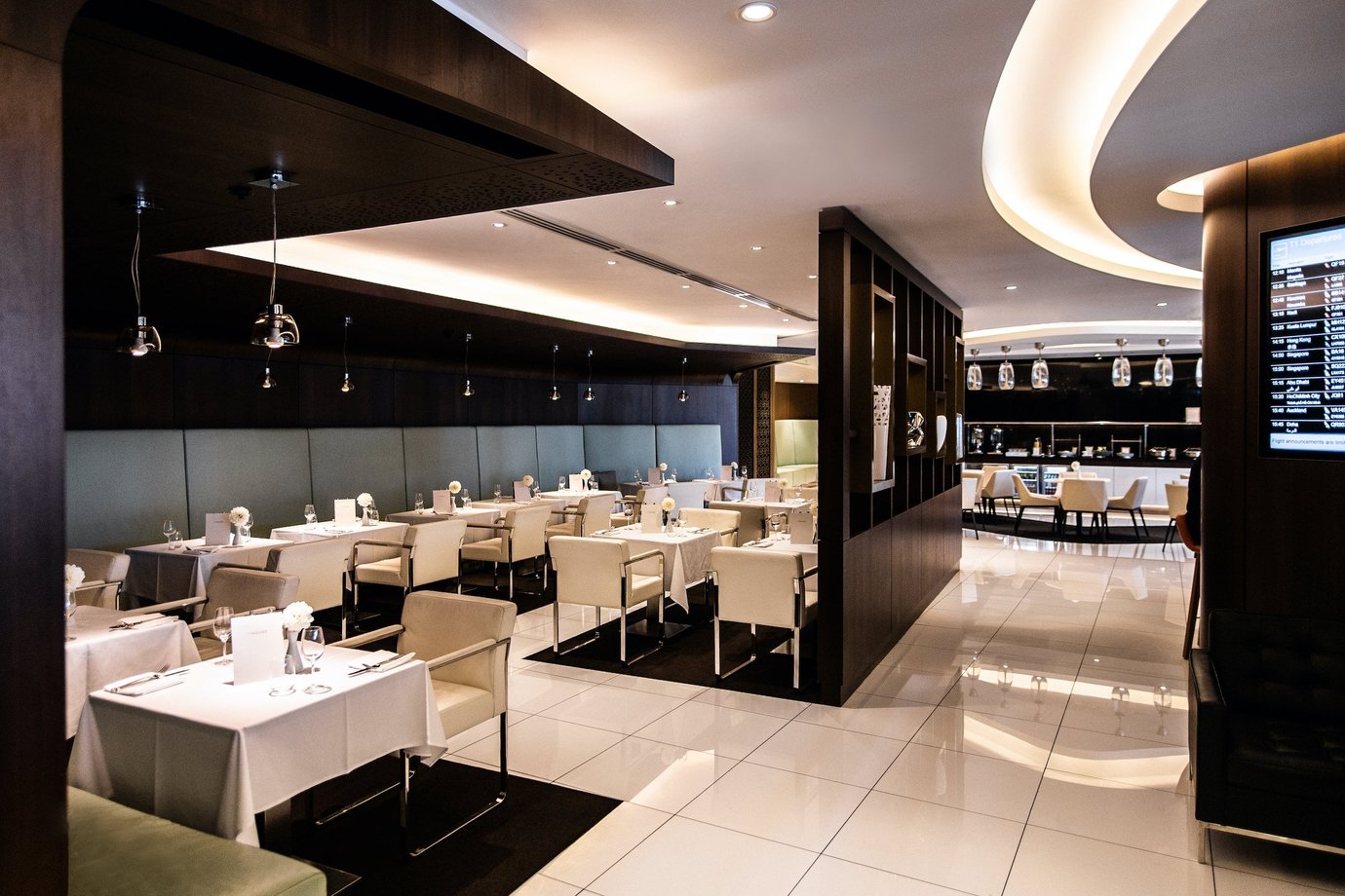 The House Lounge at Sydney Airport featuring white tablecloth, cushioned seating, dark wood finishes, and a bar area in the background.