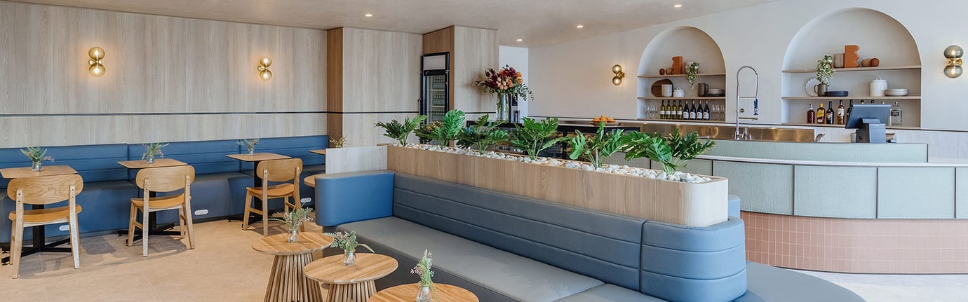 Plaza Premium Lounge at Sydney Airport arrivals area with booth seating, wooden tables, indoor greenery, and a bar and dining space in the background.