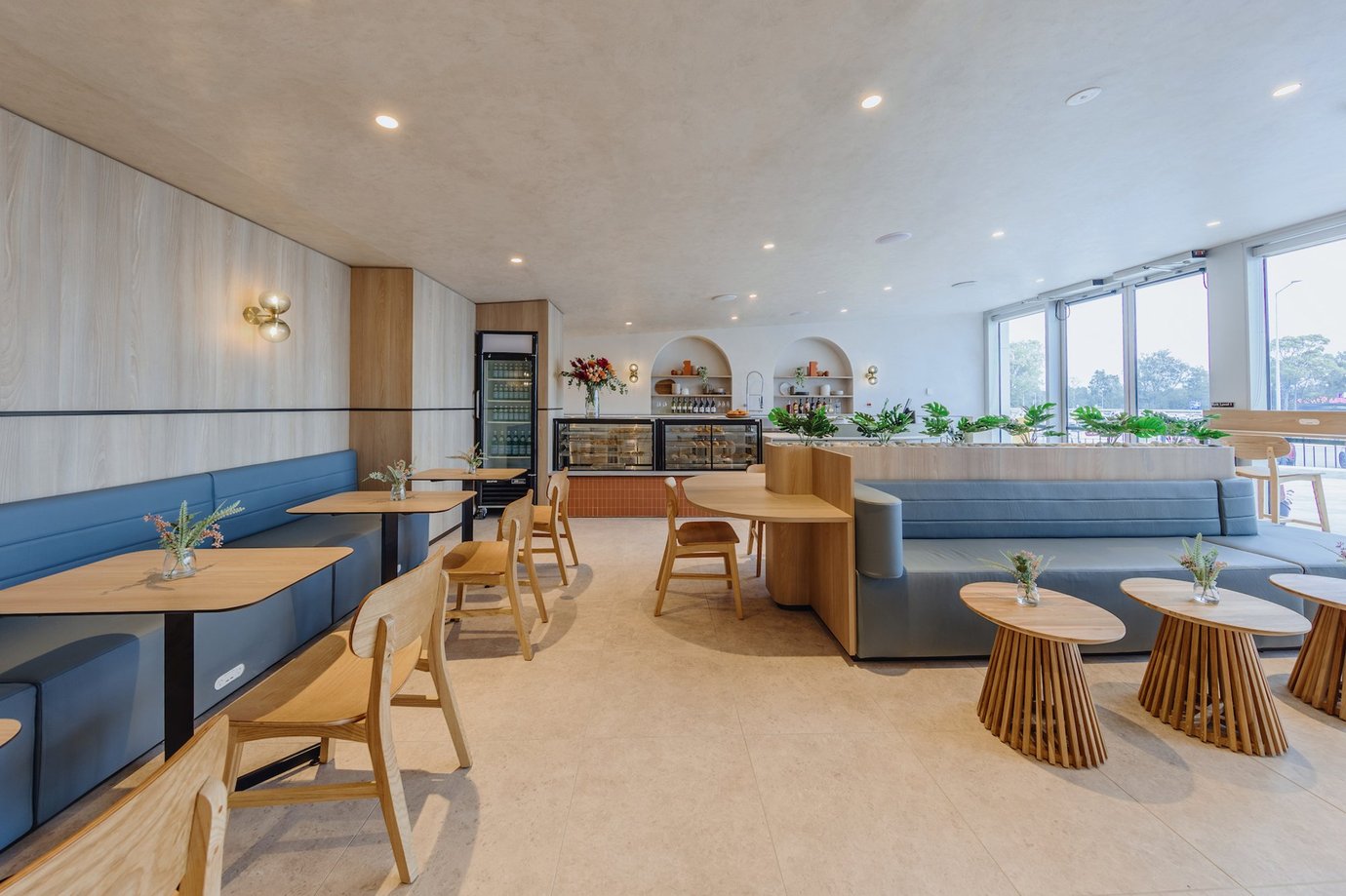 Plaza Premium Lounge at Sydney Airport arrivals seating area with booth seating, wooden tables, indoor plants, and café-style dining space.
