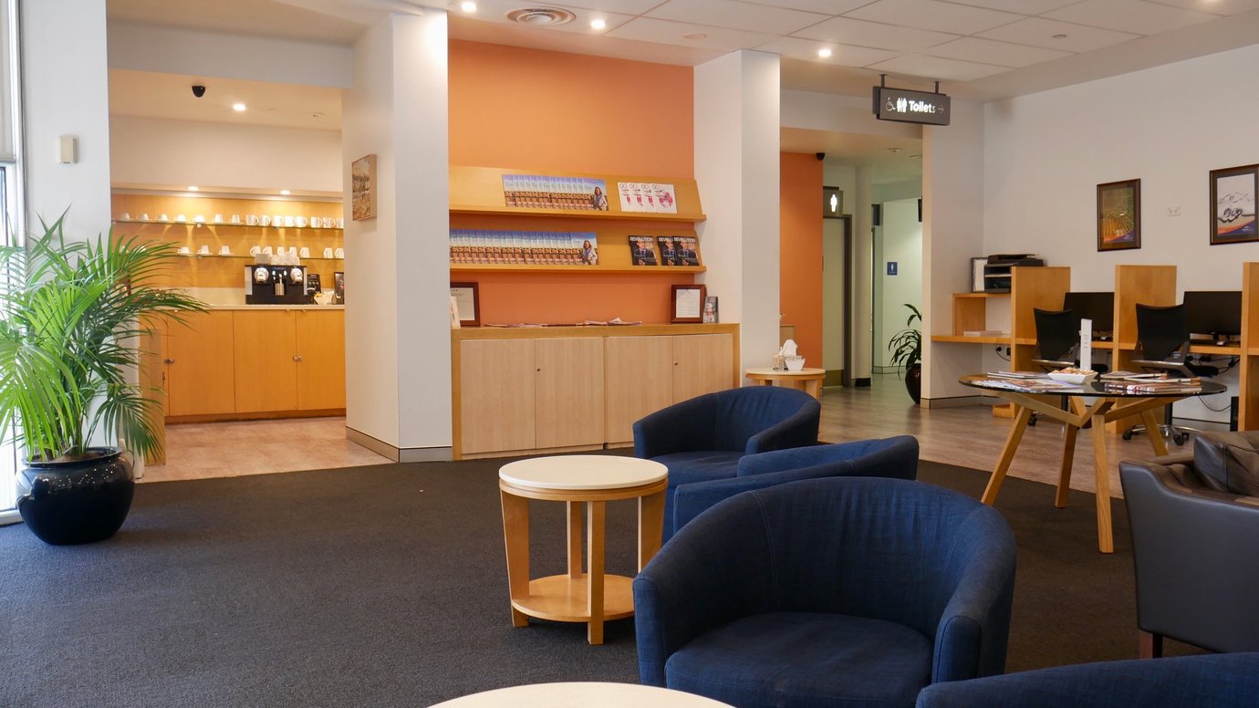 REX Lounge at Sydney Airport seating area with armchairs, coffee station, workstations, and reading materials in a relaxed space.