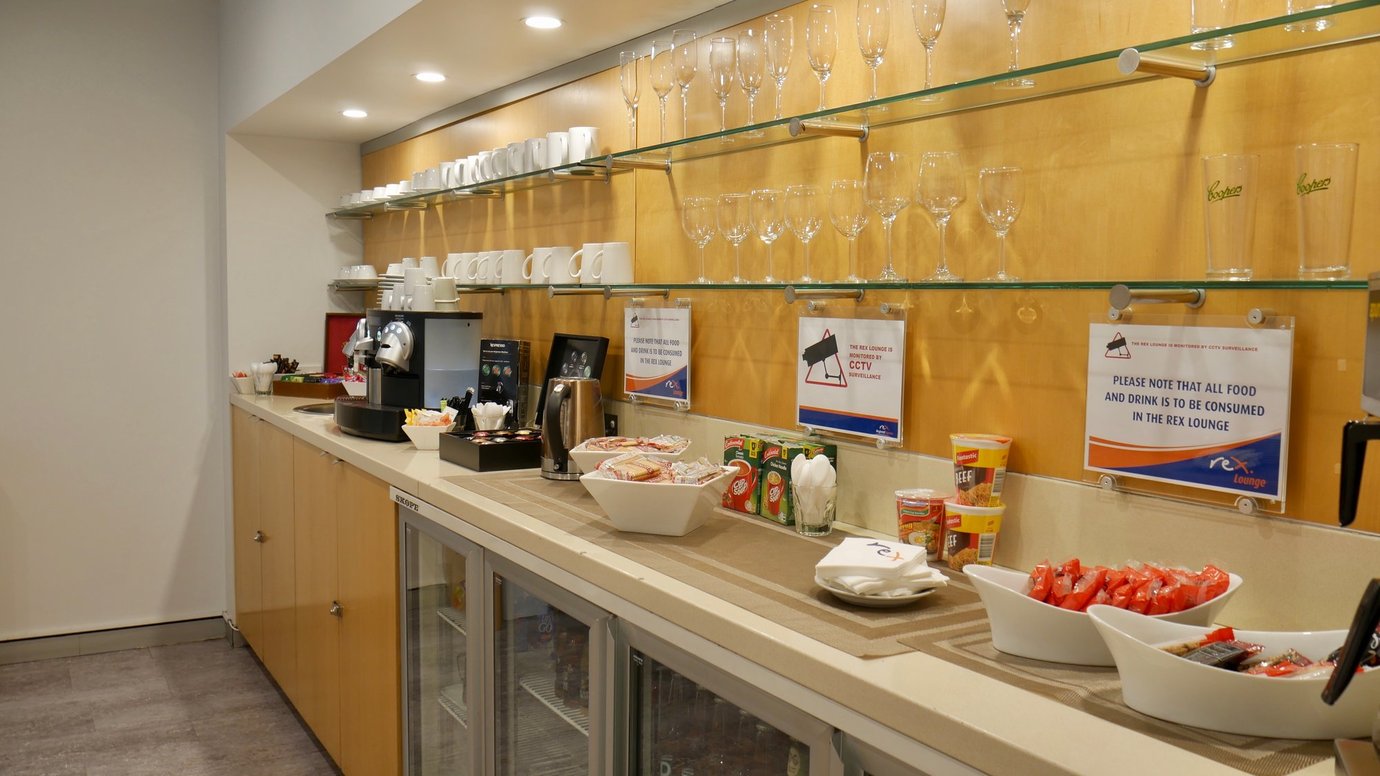 REX Lounge at Sydney Airport self-service refreshment area with coffee machine, snacks, drinks, and glassware on display shelves.