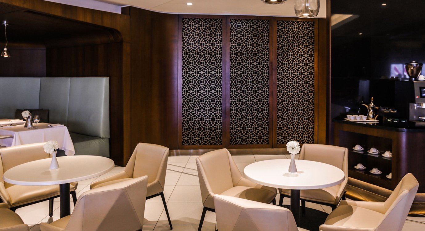 The House lounge at Sydney Airport dining area with round tables, beige seating, booth seating, and a coffee station set against dark wood interiors.