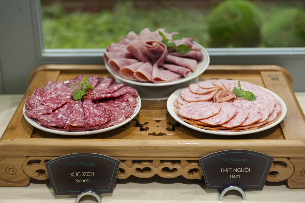 Cold cuts station at Le Saigonnais Lounge with plates of salami and sliced ham arranged on a wooden display.