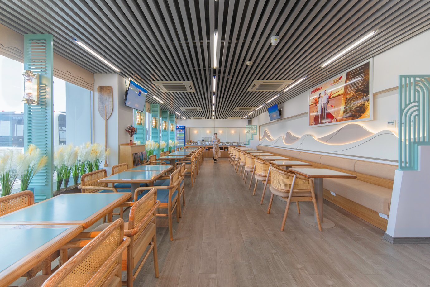 SH Premium Lounge dining area with teal tables, cane chairs, long banquette seating, and bright runway-side windows at TBB Airport. SH Premium Lounge dining area with teal tables, cane chairs, long banquette seating, and bright runway-side windows at TBB Airport.